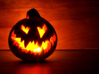 Halloweenowa dynia z wyciętą przerażającą twarzą i podświetlona od wewnątrz migotliwą świeczką.